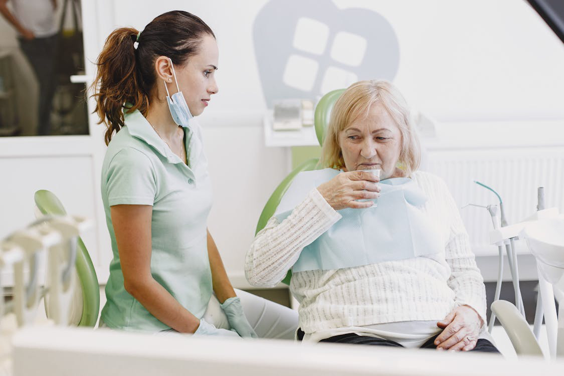 A dental nurse assisting an elderly woman drinking water in a dental clinic.