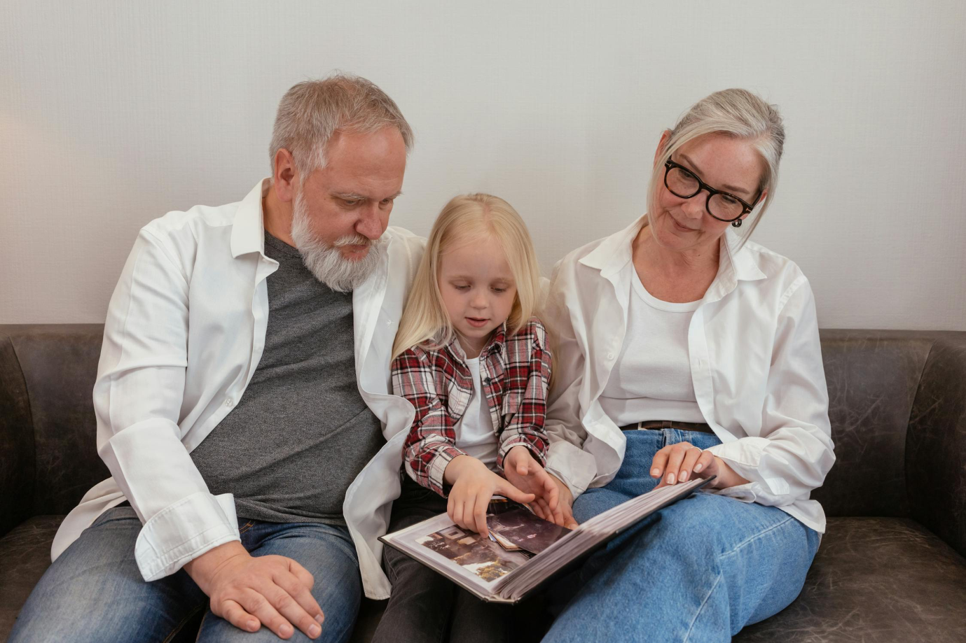 Grandparents sitting on a couch reading a book with their granddaughter at home.