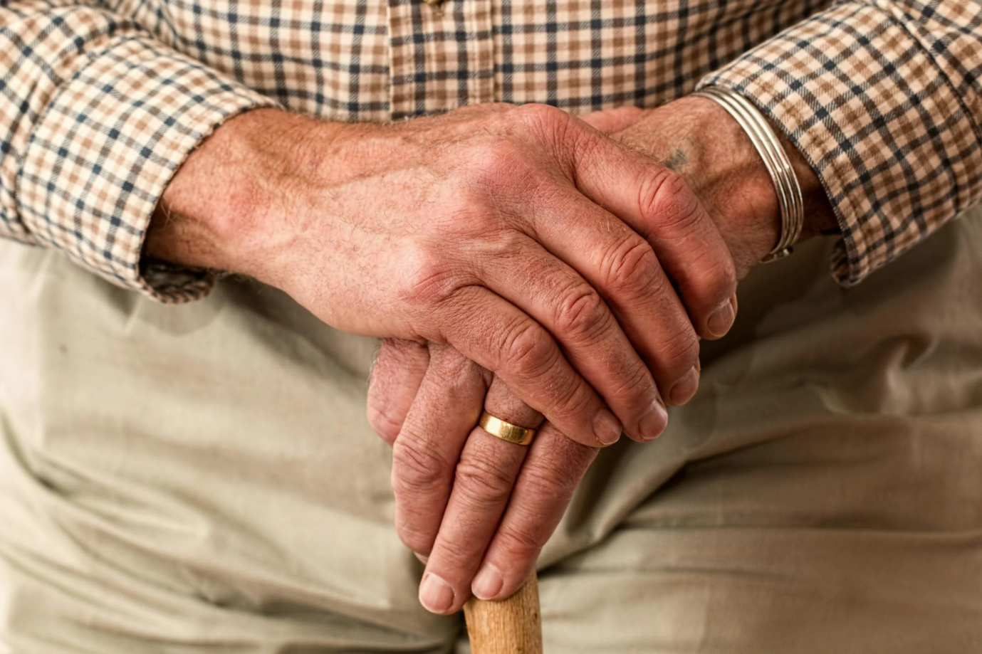 A veteran holding a walking stick with both hands clasped over it